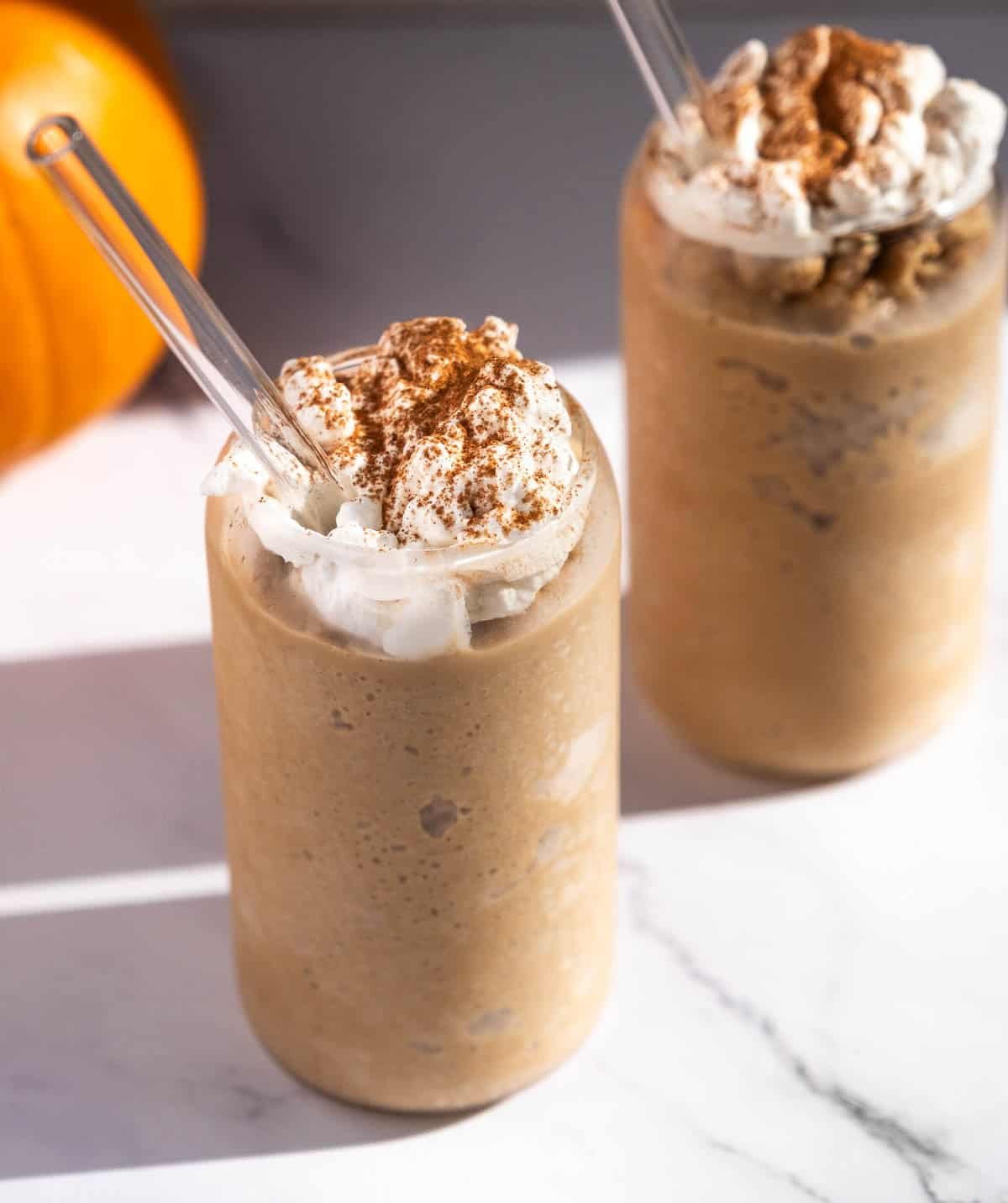 Two Pumpkin Spice Latte Slushies on a table topped with whipped cream and pumpkin pie spice seasoning.