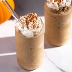 Square image showing a pumpkin spice latte slushie with a glass straw.