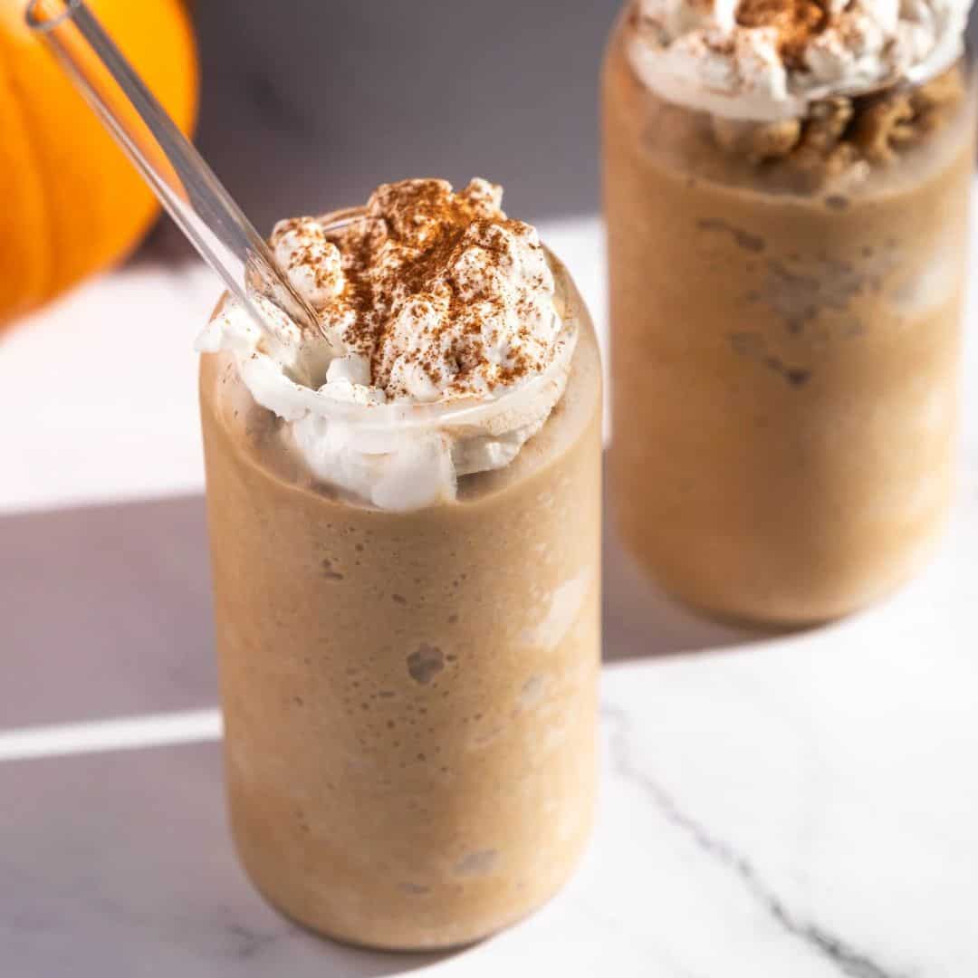 Square image showing a pumpkin spice latte slushie with a glass straw.