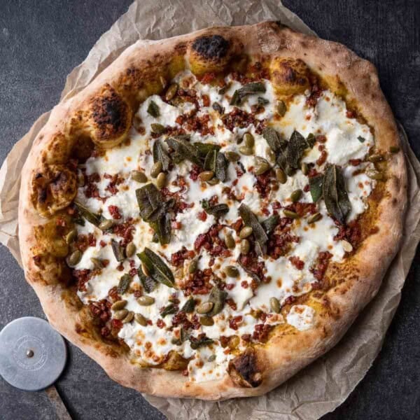 A pumpkin fall pizza on a cutting board.