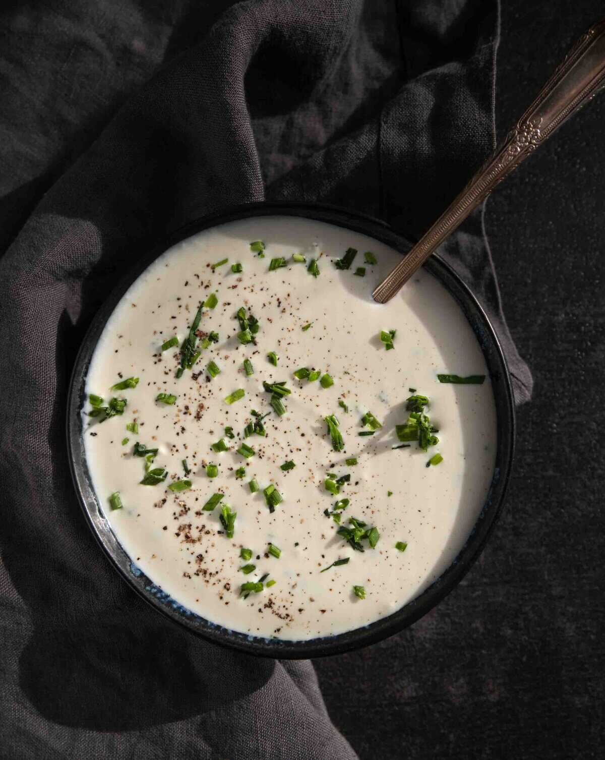 A bowl of creamy horseradish sauce with a spoon. The sauce is topped with fresh chopped chives.