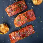 Four files of grilled salmon topped with Gochujang sauce on a black serving platter.