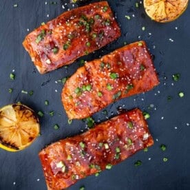 Four files of grilled salmon topped with Gochujang sauce on a black serving platter.