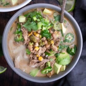 A bowl of White Chicken Chili with Poblano Peppers topped with fresh cilantro, cheese, avocado, and jalapeño slices.