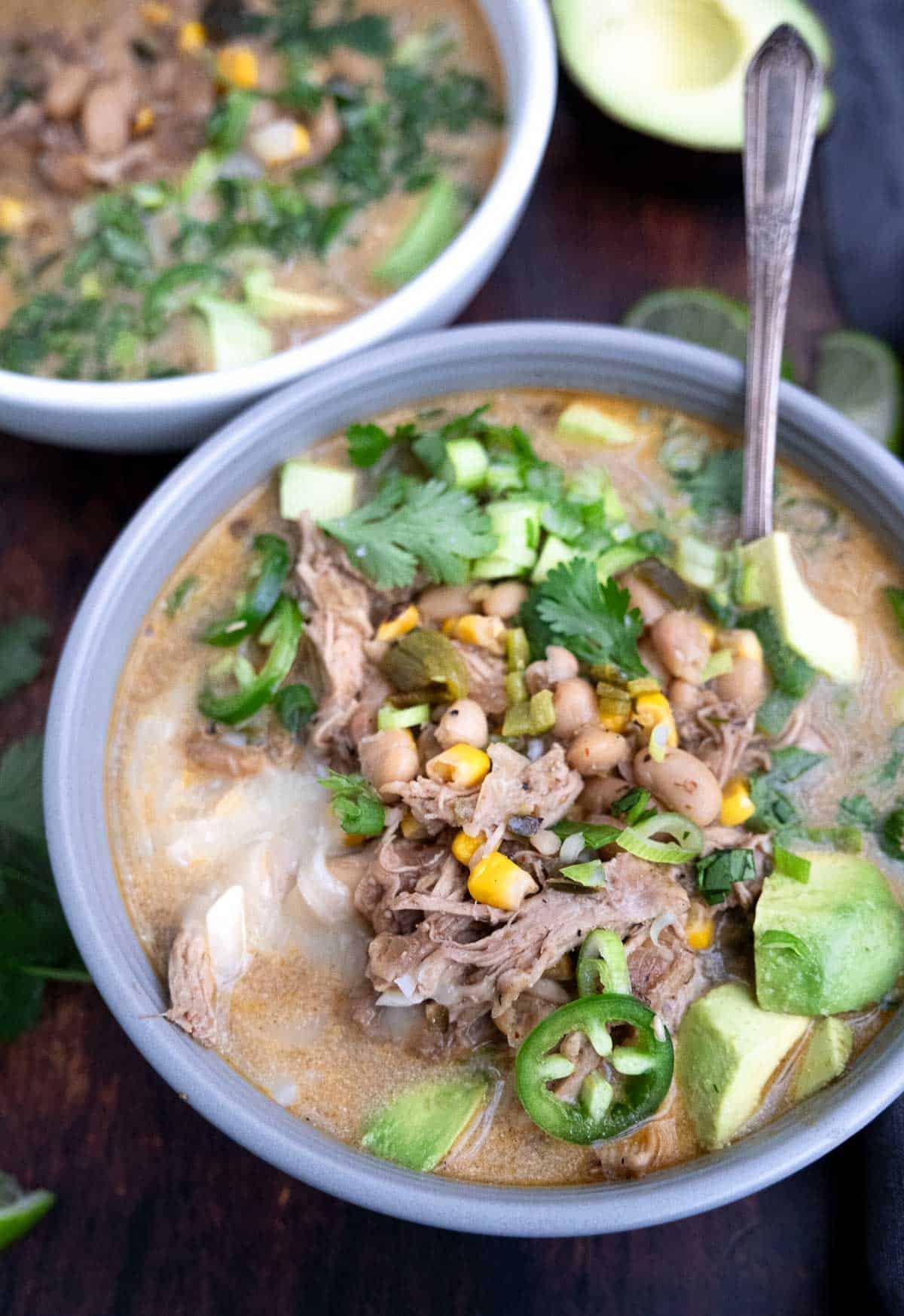 A bowl of white chicken chili with poblano peppers topped with fresh chives, jalapeno slices, and avocado.
