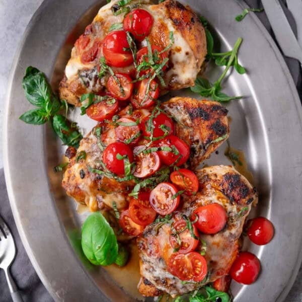 Three Grilled Chicken Margherita servings on a platter topped with sliced cherry tomatoes and fresh basil.