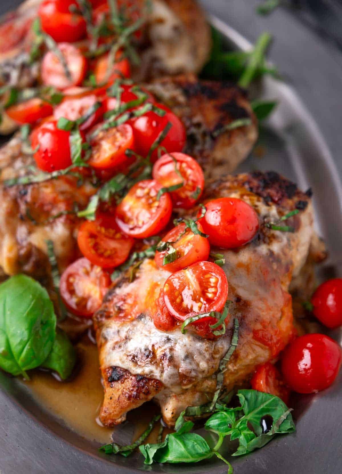 Slices of grilled chicken margherita on a platter topped with fresh tomatoes and basil.