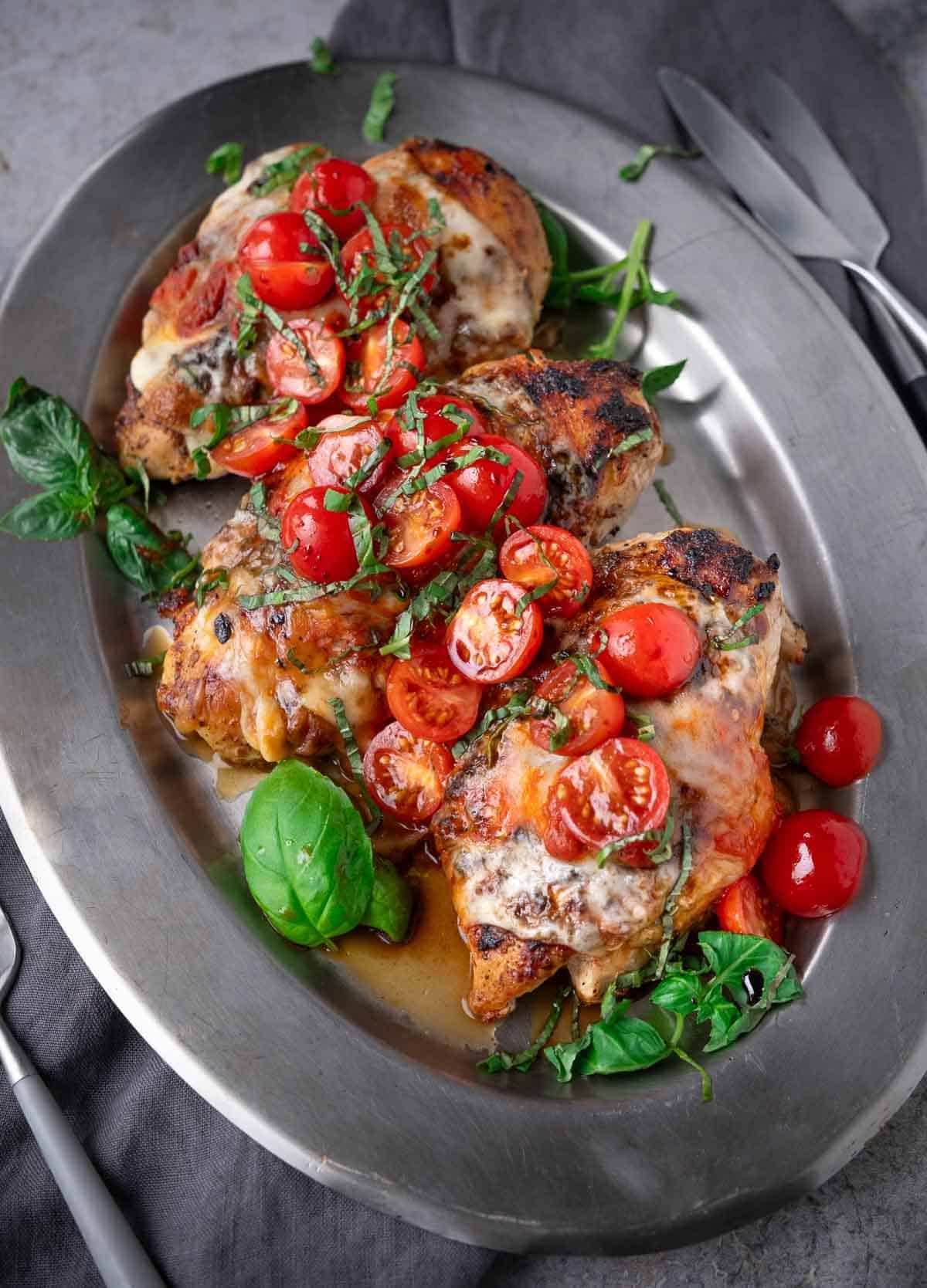 Three pieces of Grilled Chicken Margherita (with no pesto) on a platter topped with basil and cherry tomatoes.
