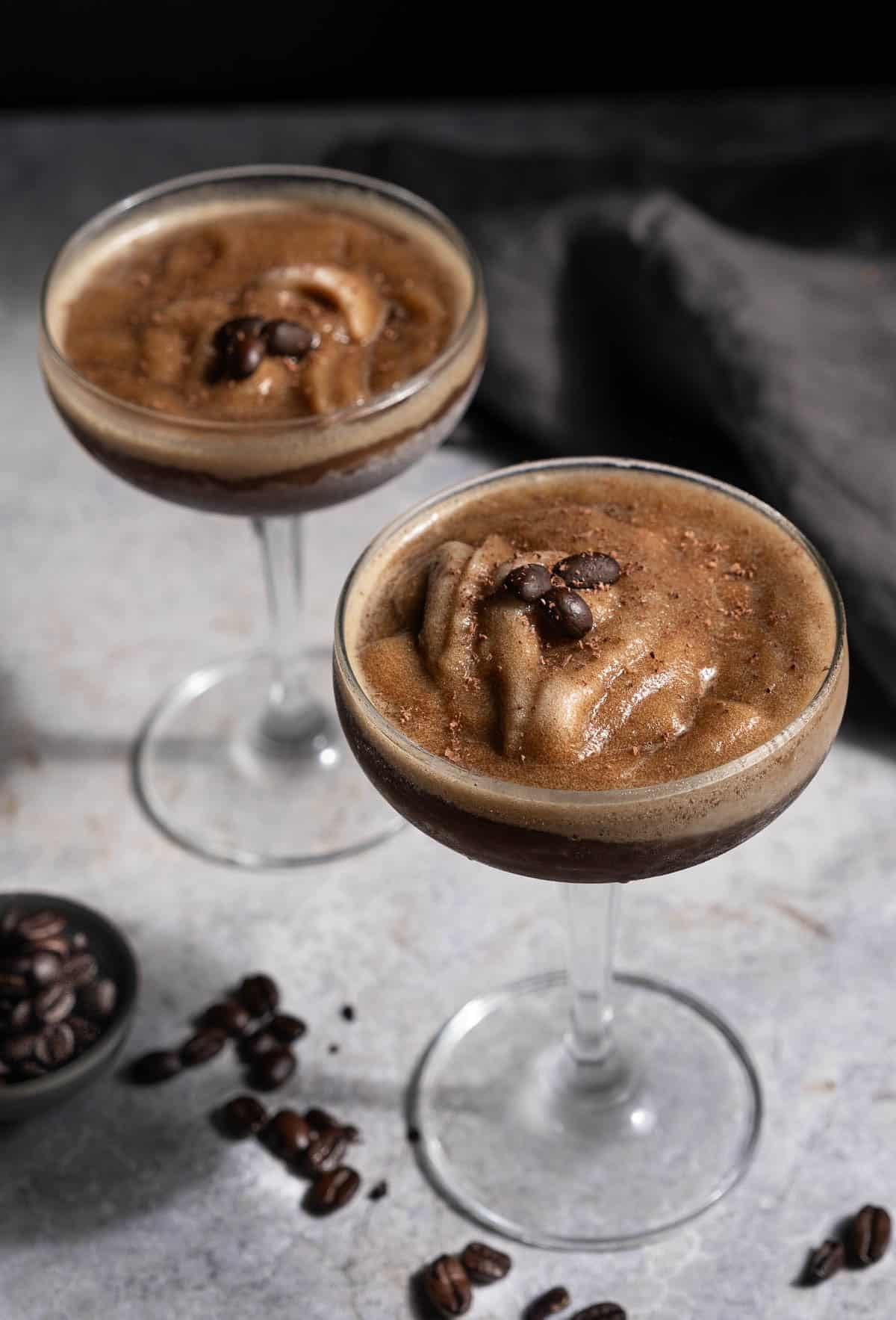 Two Espresso Martini Slushies (made in a Ninja Slushi Machine) in coupe glasses topped with espresso beans.
