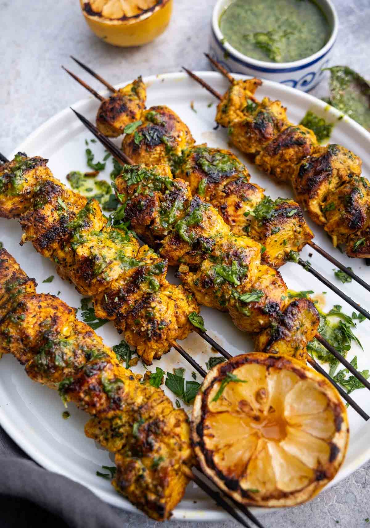 Moroccan Chicken Skewers on a platter topped with a herb garlic sauce.