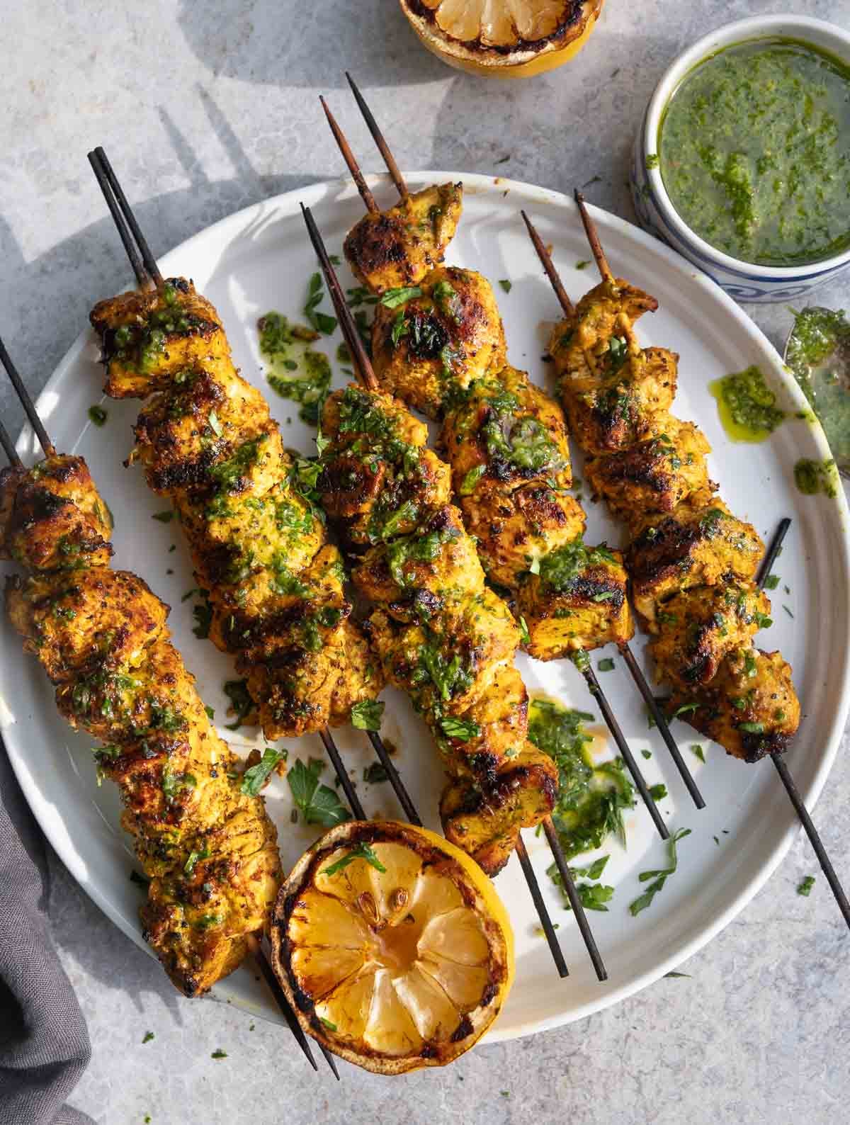 Moroccan Chicken Skewers on a serving platter served with a green garlic lemon herb sauce. 