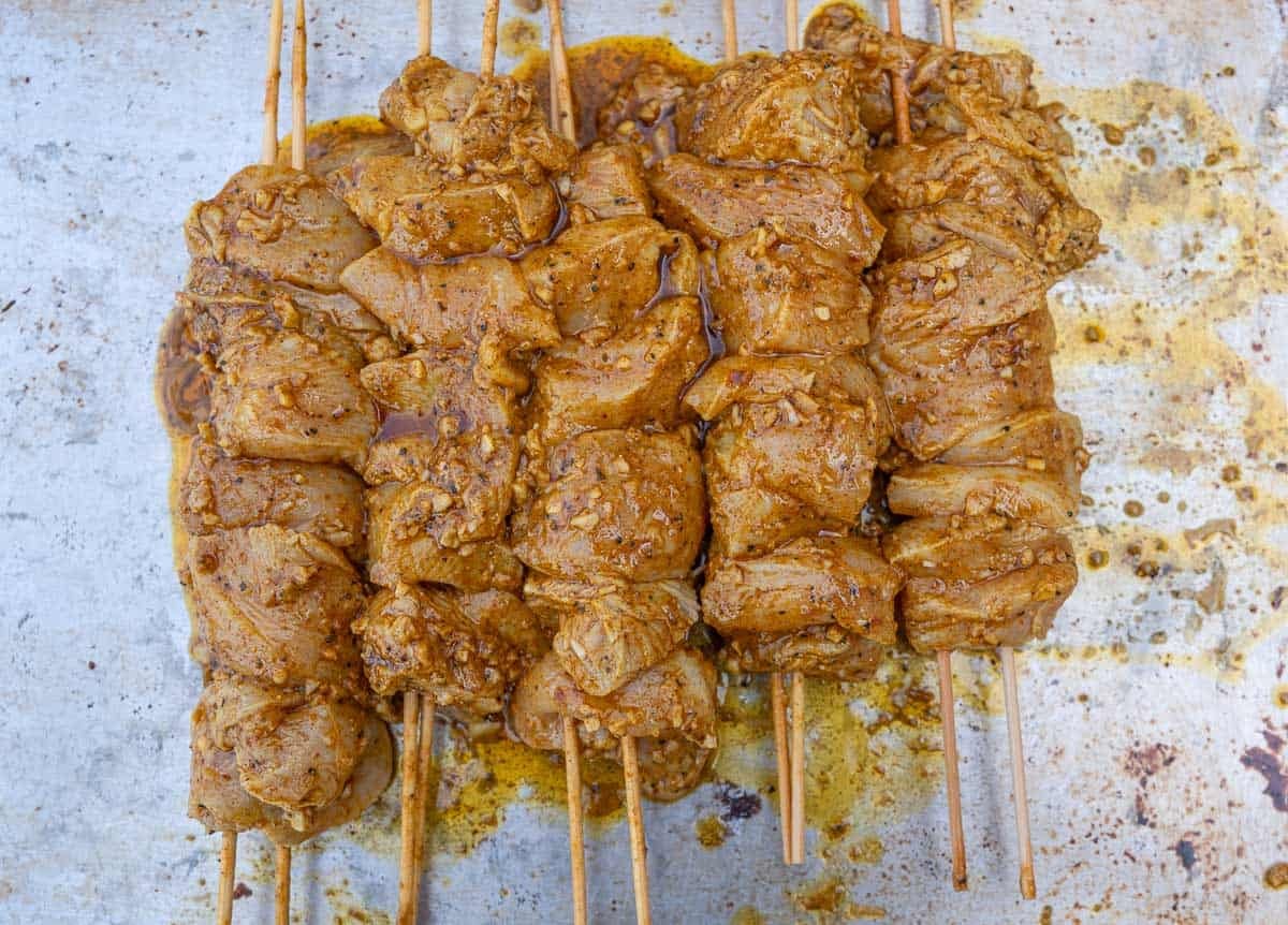 Marinated raw chicken arranged on skewers in a glass dish.