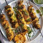 Moroccan Chicken Skewers on a platter topped with a fresh green herb sauce.