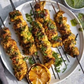 Moroccan Chicken Skewers on a platter topped with a fresh green herb sauce.