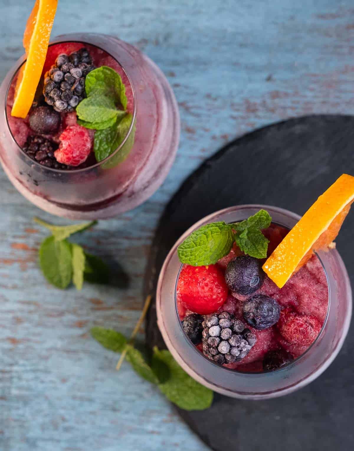 A top down view of two Red Wine Sangria Slushies topped with frozen berries and a slice of orange.