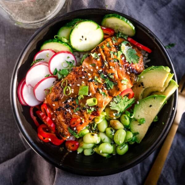 Grilled Miso Glazed Salmon served in a bowl over rice with cucumber, radishes, edamame, and avocado slices.
