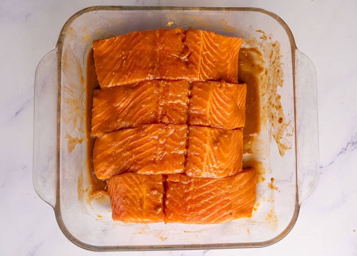 Four slices of salmon in a glass dish marinating in a miso marinade.